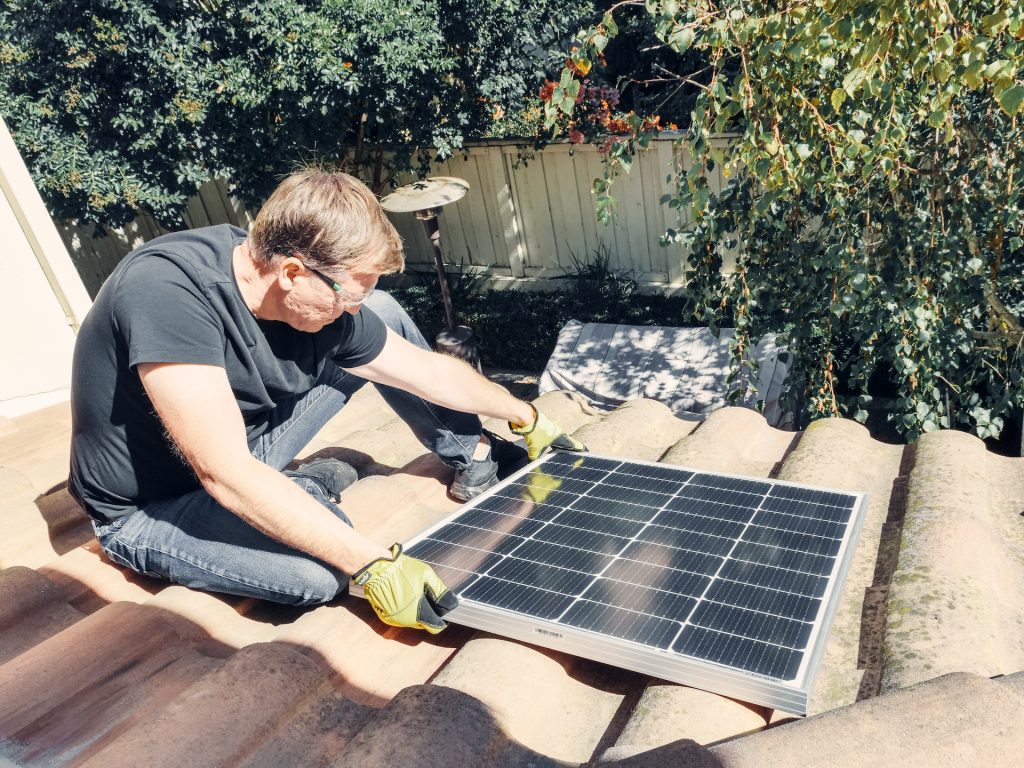 A Man in Black Shirt Sitting on the Roof while Holding a Solar Panel